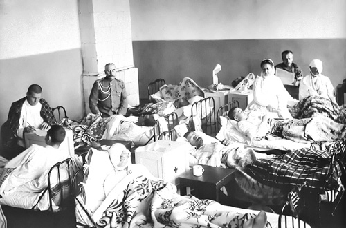 Персонал и раненые в одной из палат Серафимовского лазарета. У кровати раненого сидят завхоз лазарета капитан С.П.Васильев, на заднем плане читает газету санитар-доброволец В.А.Панасюк. Фото 1914 г.